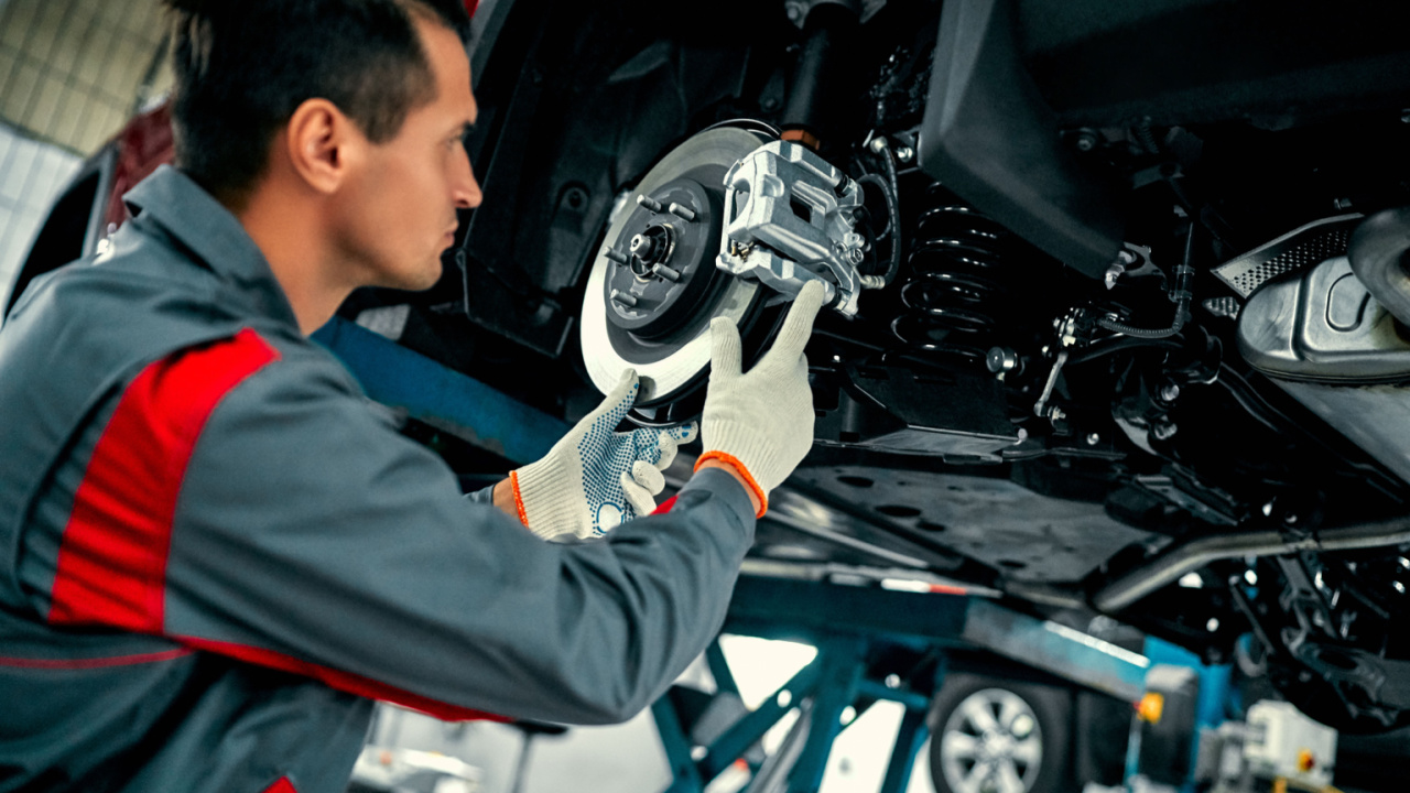 Car mechanic worker repairing suspension of lifted automobile at auto repair garage shop station