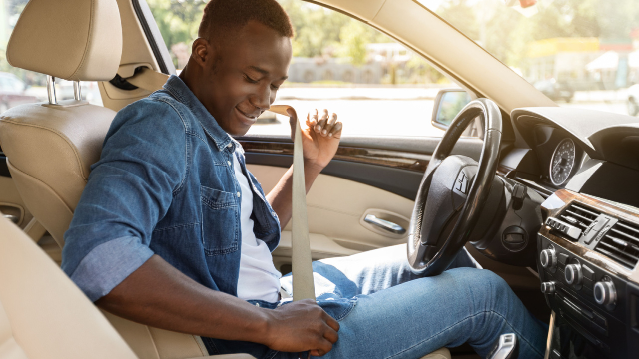 Safe driving concept. Positive young black man fastening car seat belt, side view, copy space. Cheerful african american guy beginning car trip, renting nice cozy auto for travelling