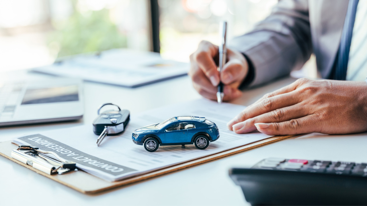 Man signing car insurance document or lease paper. Writing signature on contract or agreement. Buying or selling new or used vehicle. Car keys on table. Warranty or guarantee. Customer or salesman.