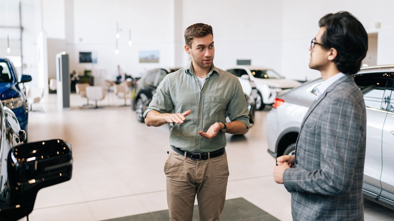 Portrait of serious male client talking to professional car dealer in business suit in dealership discussing automobiles looking at luxurious new model. Concept of choosing and buying new auto.