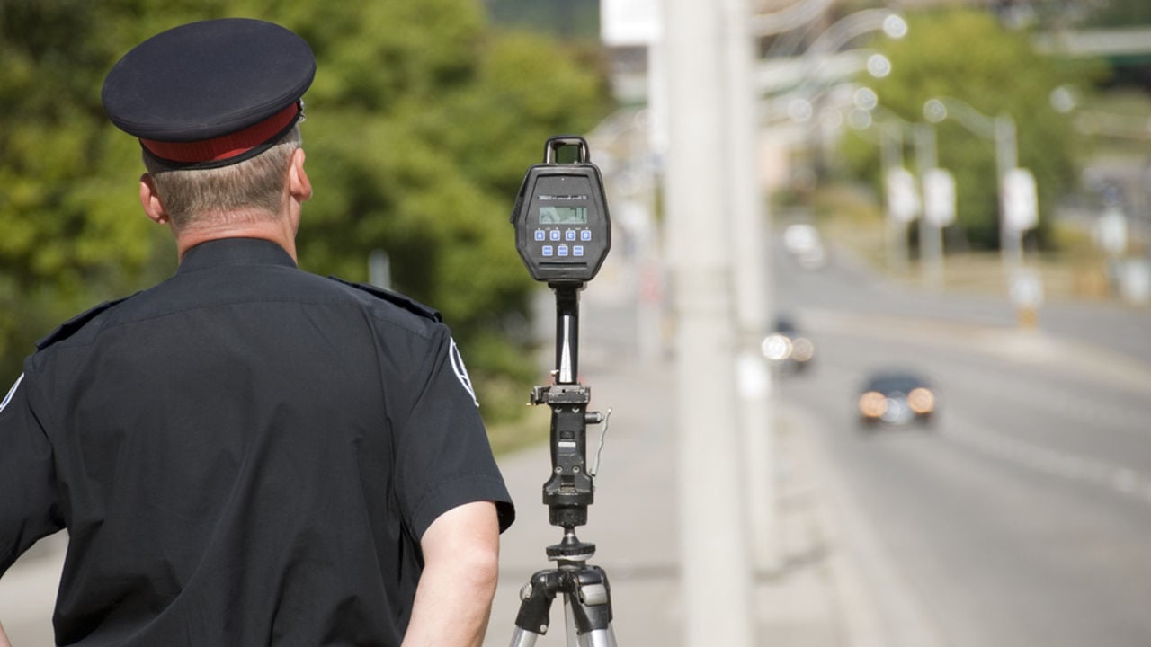 A North American policeman waits to catch speeding drivers with a radar gun. (Shot with minimum depth of field. Focus is on the police officer and radar gun.)