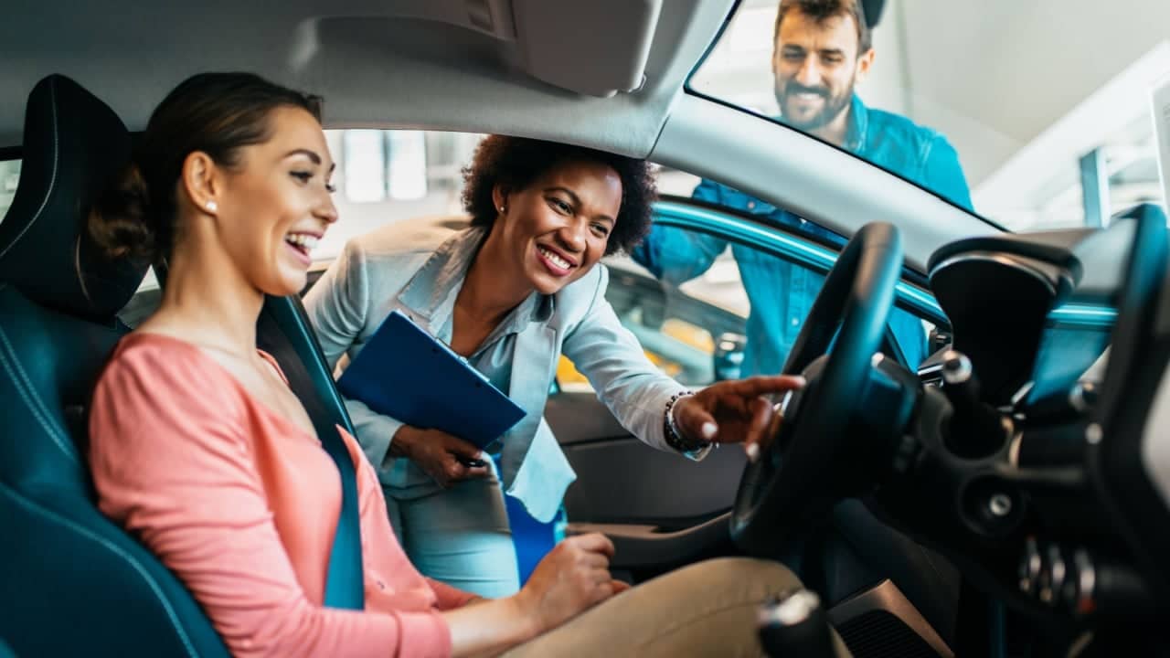 Young couple talking with saleswoman at car dealership