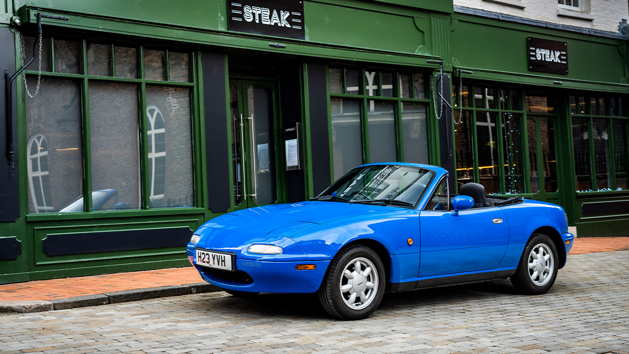 Mazda Miata NA, front 3/4 view, blue exterior, steakhouse, roof down