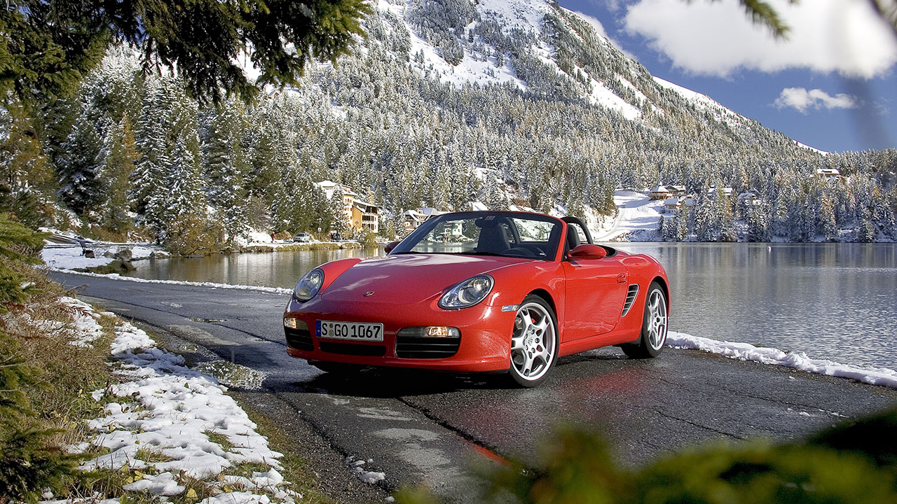 Porsche Boxster 987, front 3/4 view, red, roof down, mountain scenery.