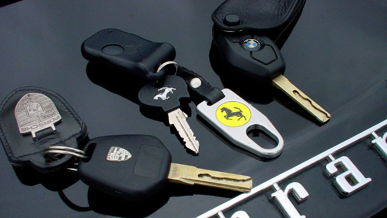 A Porsche, Ferrari, and BMW ignition key set down on a black Ferrari