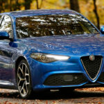 A blue Alfa Romeo Giulia Veloce driving through a forest, front 3/4 view