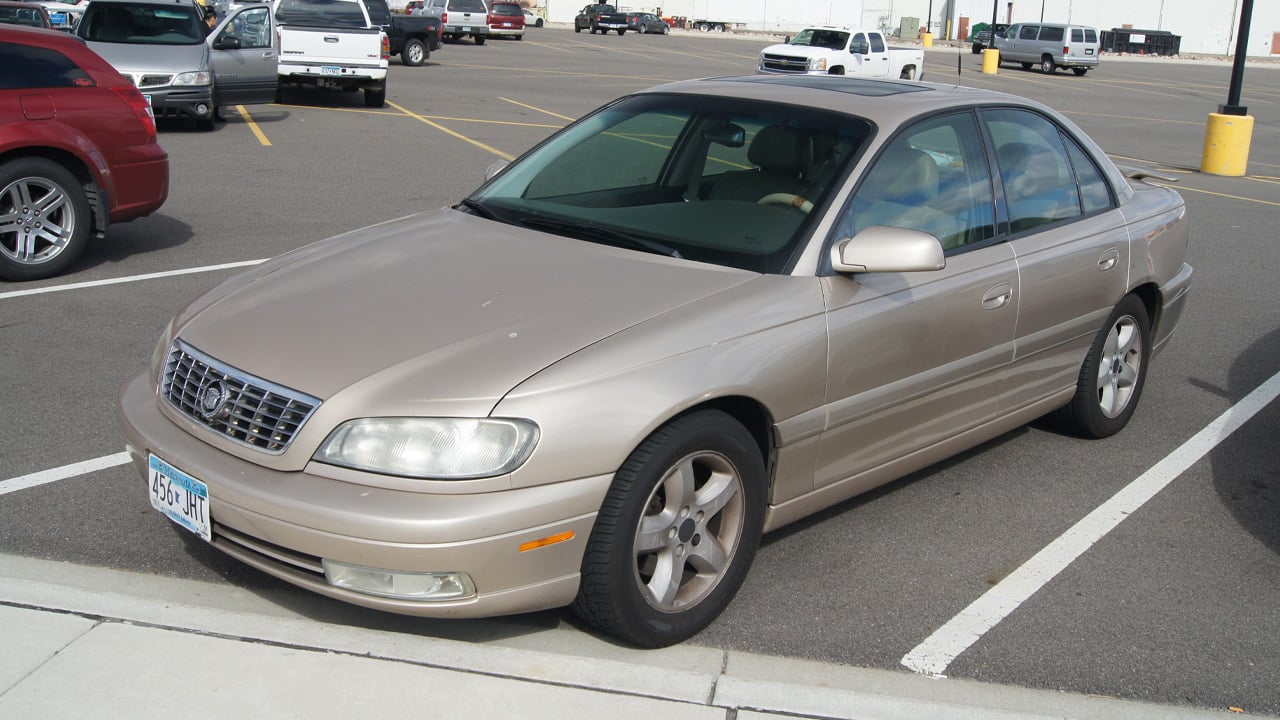 A Cadillac Catera in gold in a parking spot, front 3/4 view