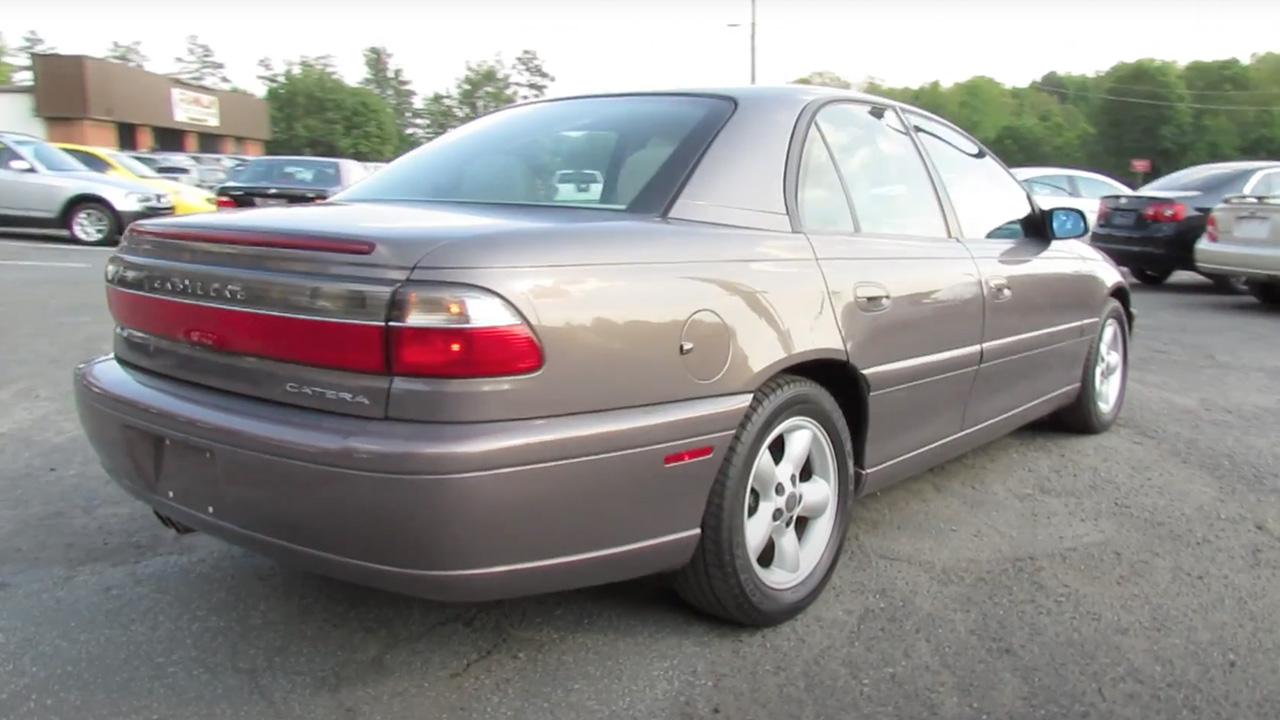 A light brown Cadillac Catera at a used car dealership, rear 3/4 view