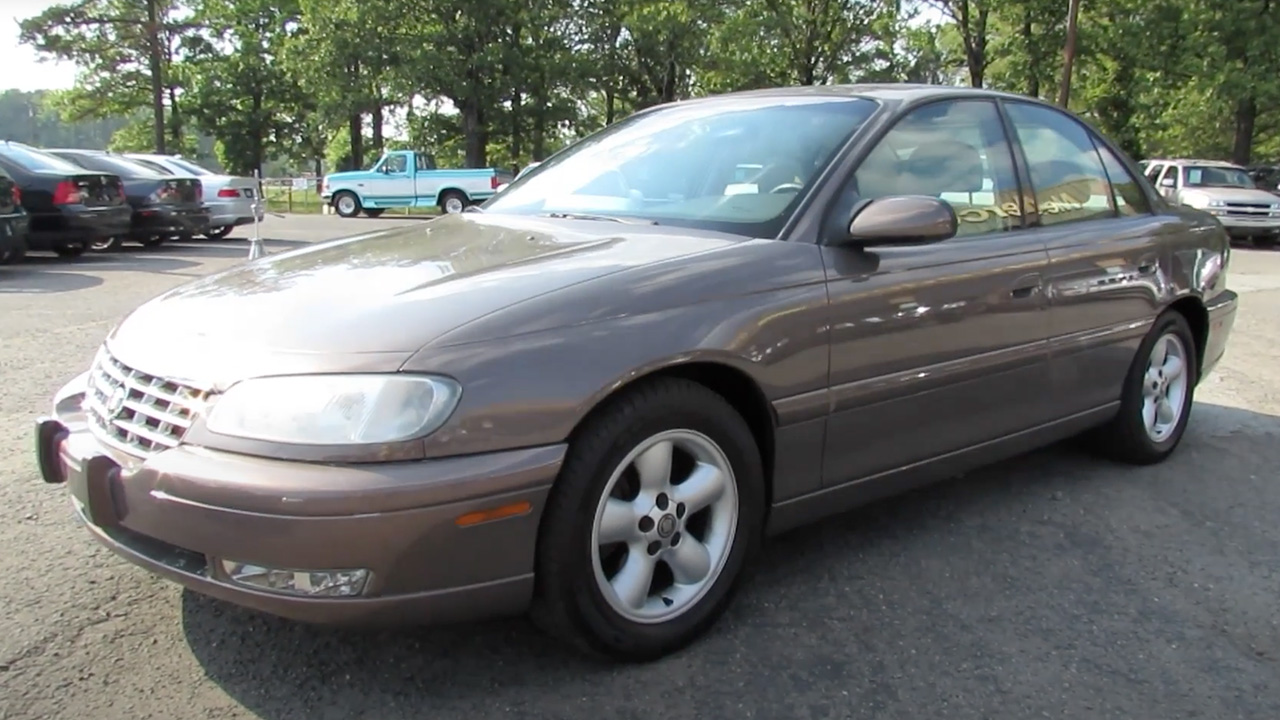 A light brown Cadillac Catera at a used car dealership, front 3/4 view