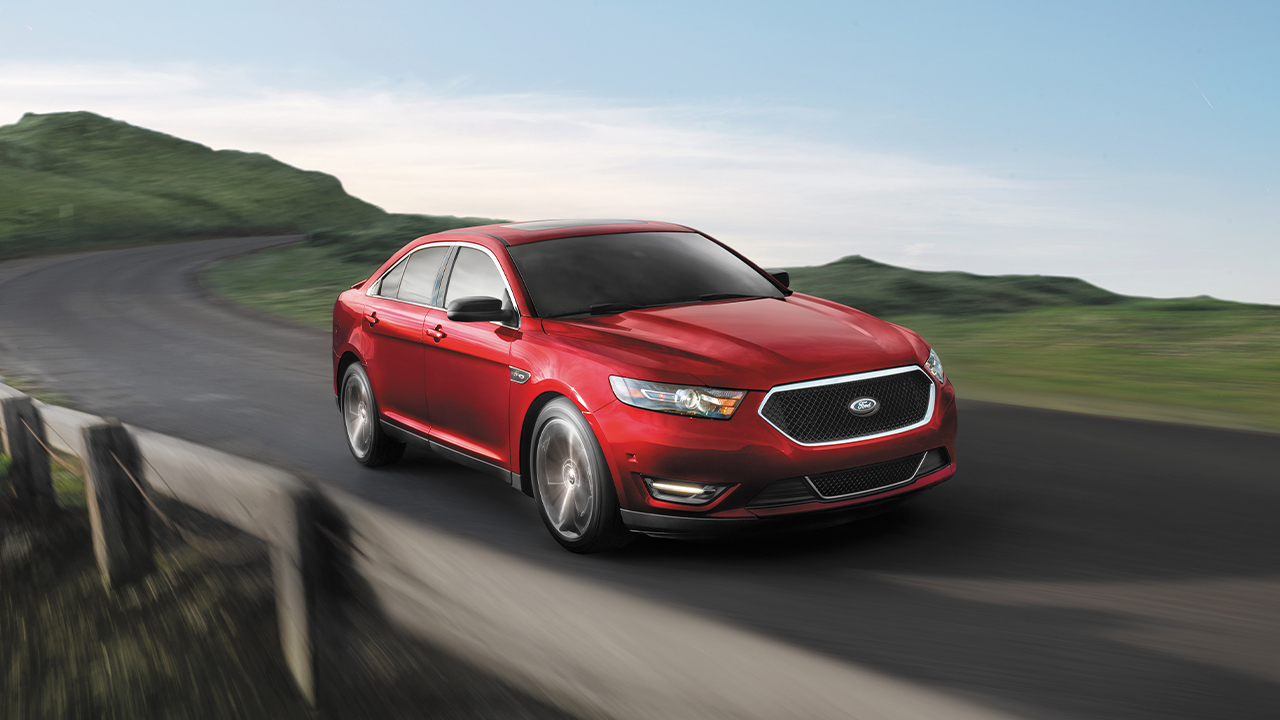 A red Ford Taurus SHO on the move on a scenic road, front 3/4 view