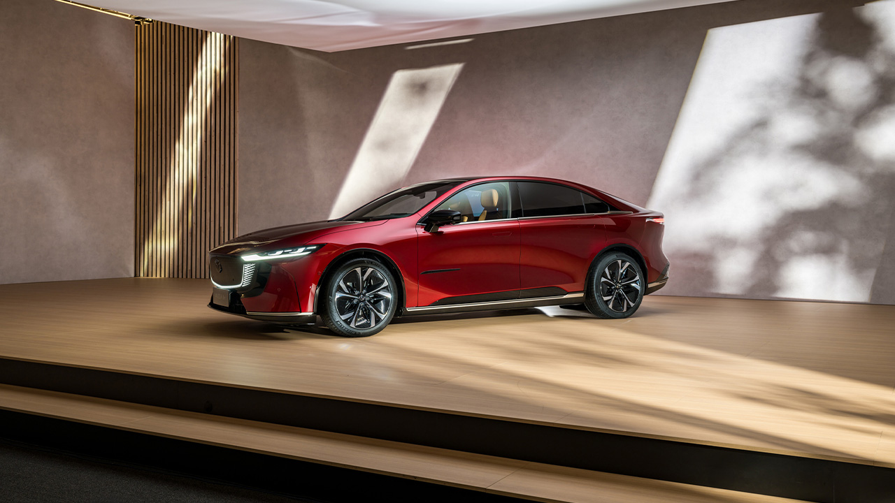 The Mazda 6e on a wooden podium, red exterior, front 3/4 view