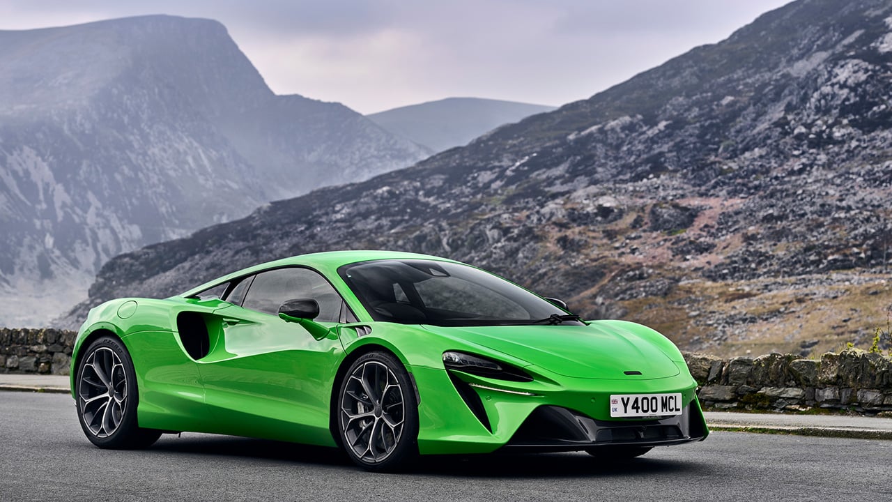 A green McLaren Artura on a mountain road, static, front 3/4 view