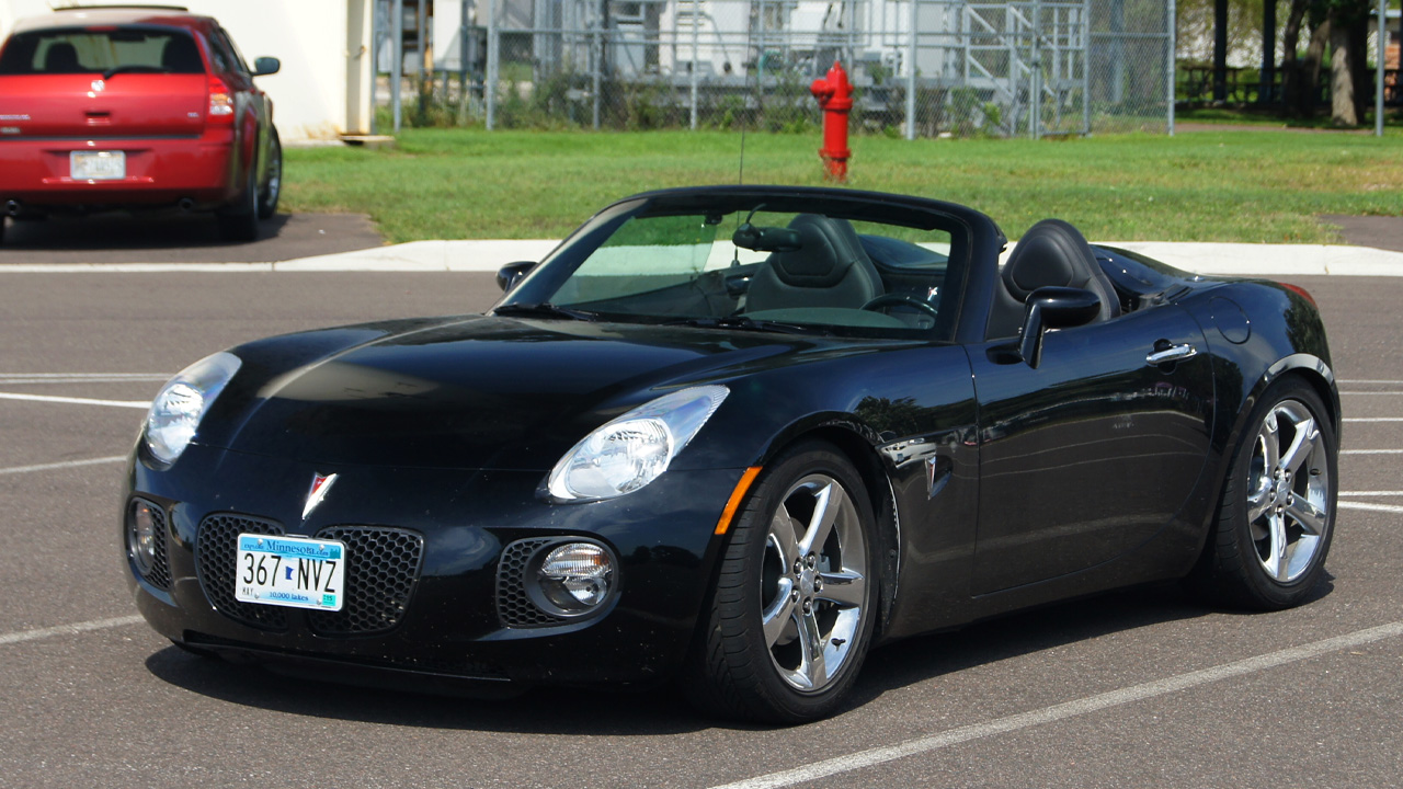 A black Pontiac Solstice GXP in a parking spot, roof down, front 3/4 view