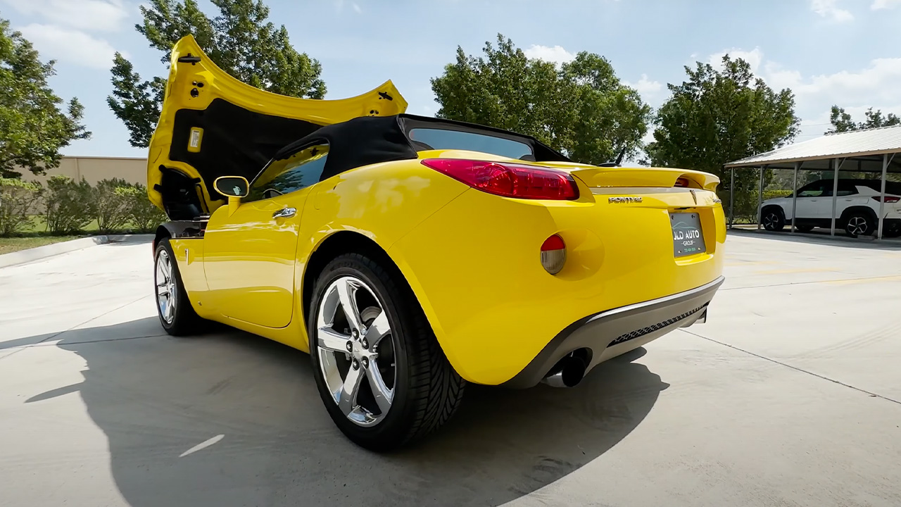 A yellow Pontiac Solstice GXP with its hood open, rear 3/4 view