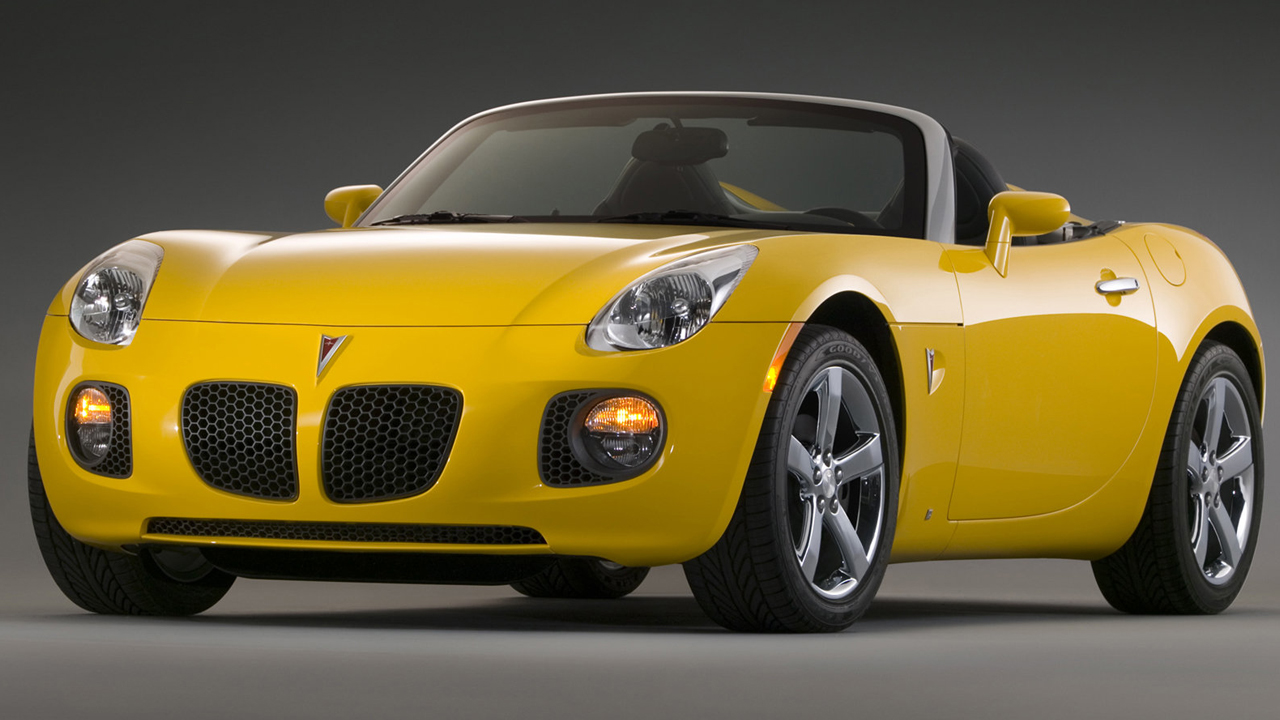 A yellow Pontiac Solstice GXP with the roof down, studio shot, front 3/4 view