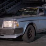 A blue Volvo 240 wagon sleeper in a garage, front 3/4 view