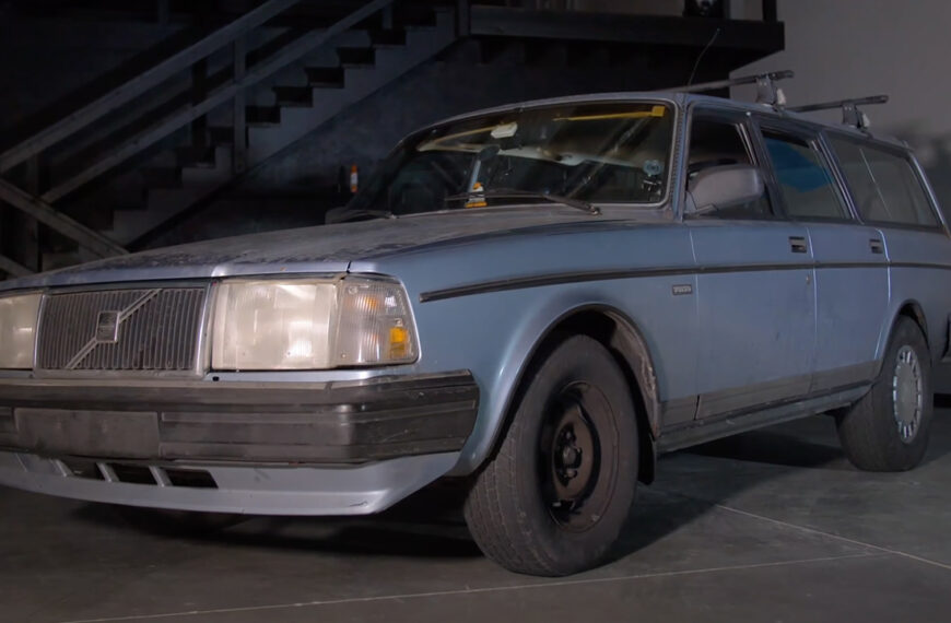 A blue Volvo 240 wagon sleeper in a garage, front 3/4 view