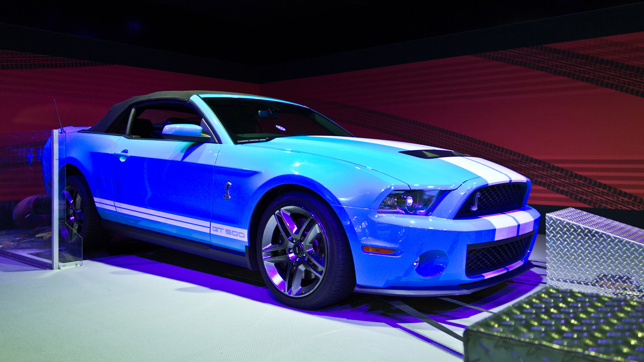 A 2013 Shelby GT500 convertible at an auto show, front 3/4 view, blue with white stripes