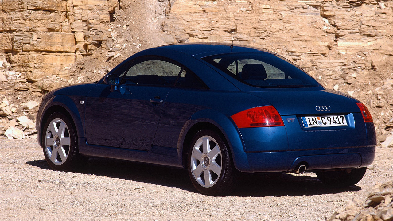 A dark blue first generation Audi TT, rear 3/4 view