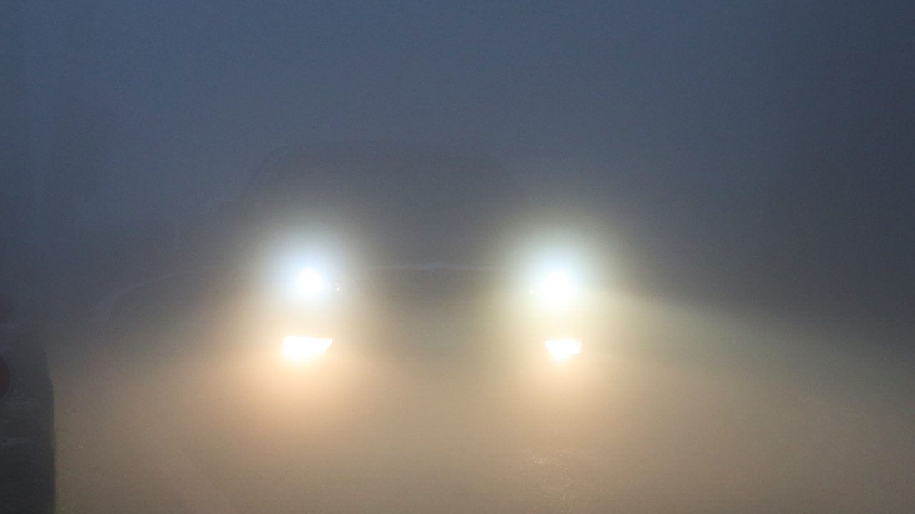 A bright set of headlights and foglights on a dark foggy day