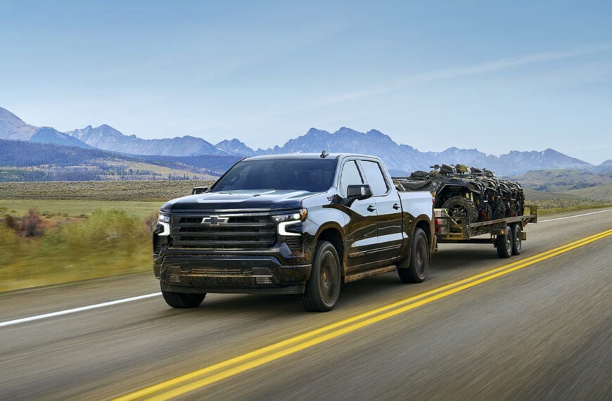 A facelifted Chevrolet Silverado 1500 in dark blue towing a trailer, front 3/4 view