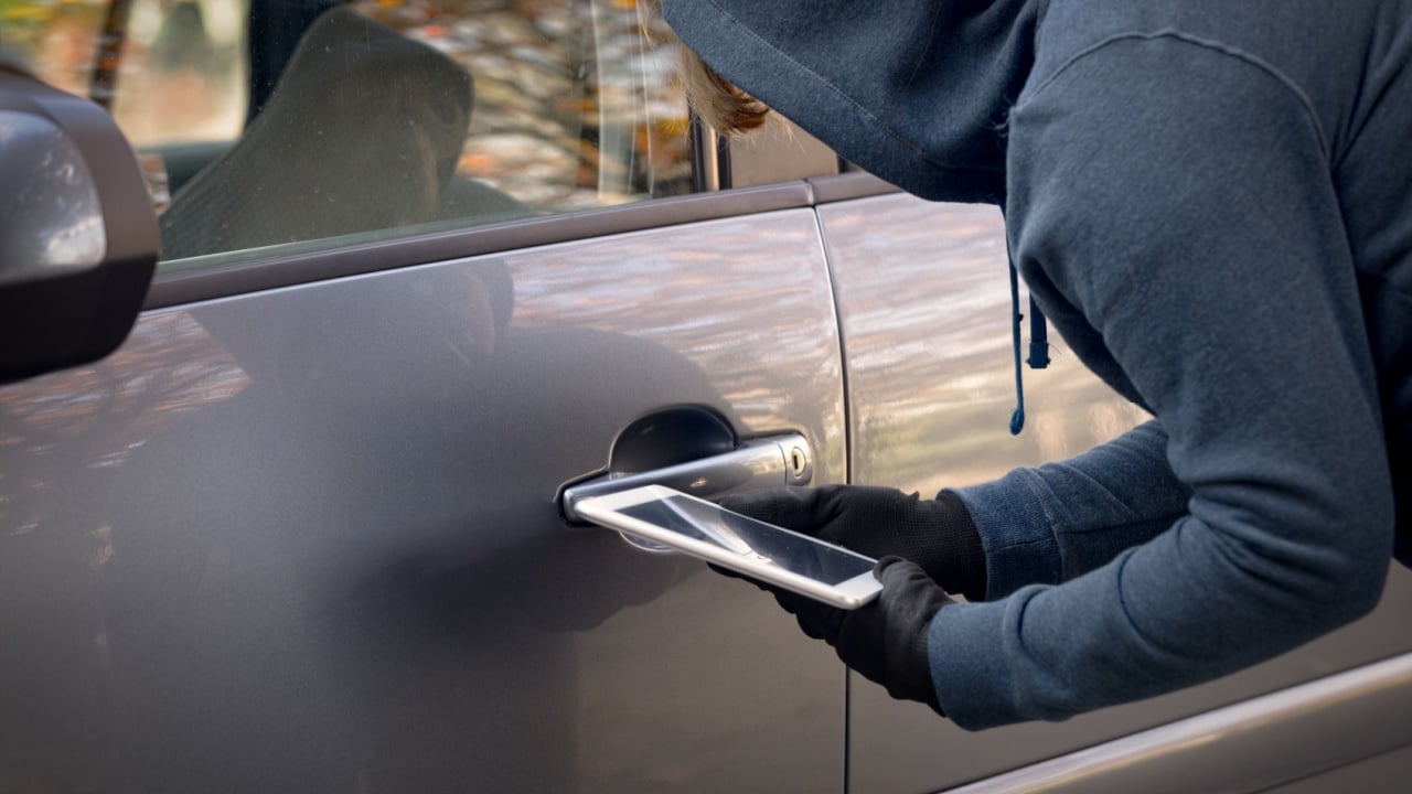 Hooded thief tries to break the car's security systems with tablet. Hacking modern car concept