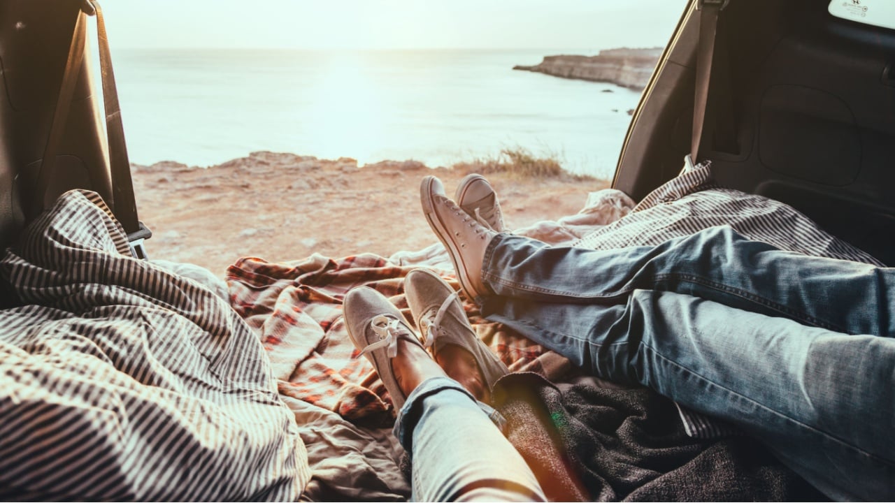 Man and woman relaxing inside trunk and watching at the sea. Fall car trip in sunset. Freedom travel concept. Autumn weekend.