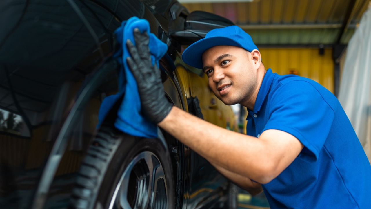 Man worker washing car service with micro fiber. Car wash cleaning wipe station. Employees clean a vehicle professionally detailing.
