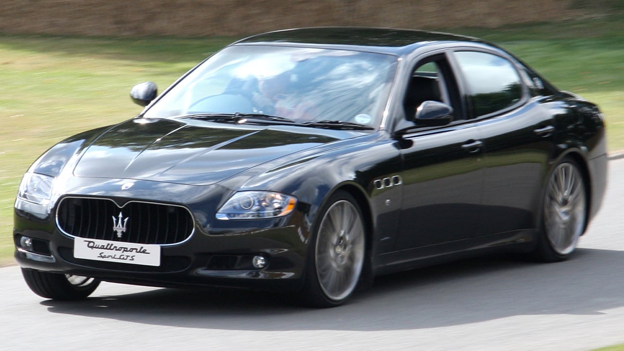 A black Maserati Quattroporte GTS driving up the Goodwood hillclimb course, front 3/4 view