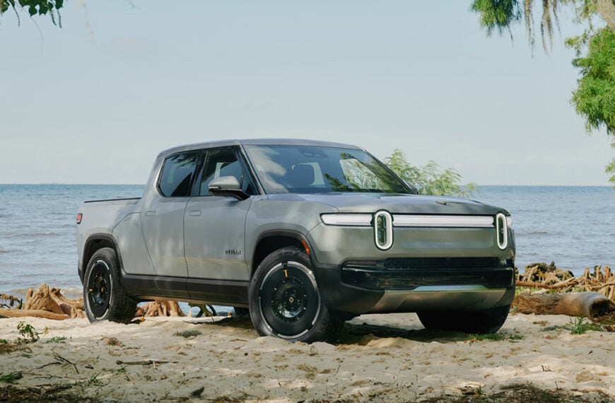 A white Rivian R1T near a beach, front 3/4 view