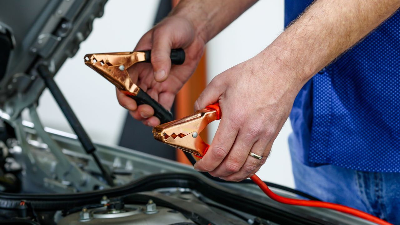 Close up hand holding jump start car cables to recharge car's battery with electricity trough jumper cables.