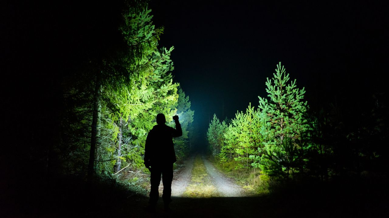 Man standing outdoor at rainy foggy night shining with flashlight.