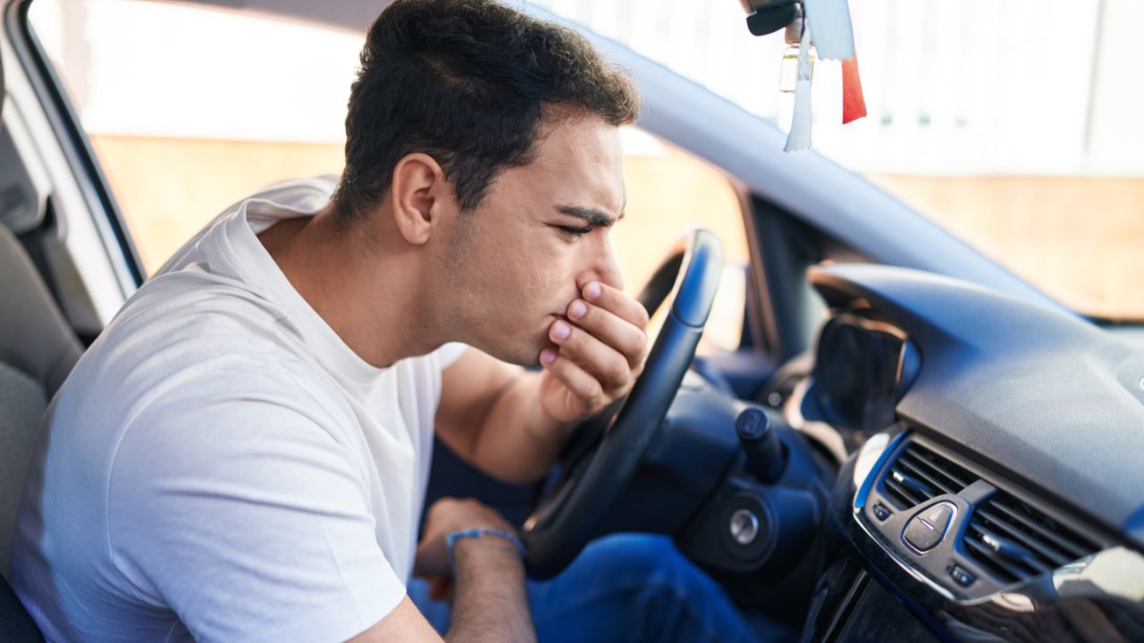 Young hispanic man smelling bad aroma sitting on car at street