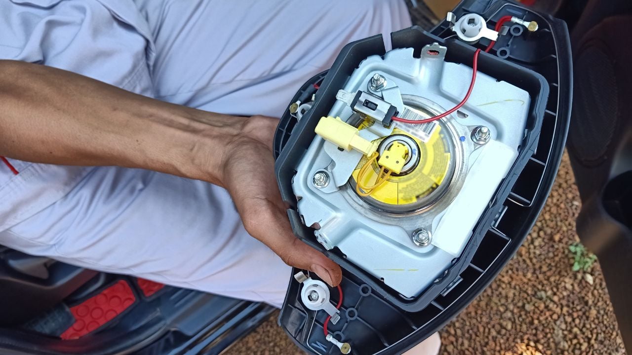 the technician in uniform holding the airbag panel that take off from the steering wheel in passenger cabin of the car between onsite service