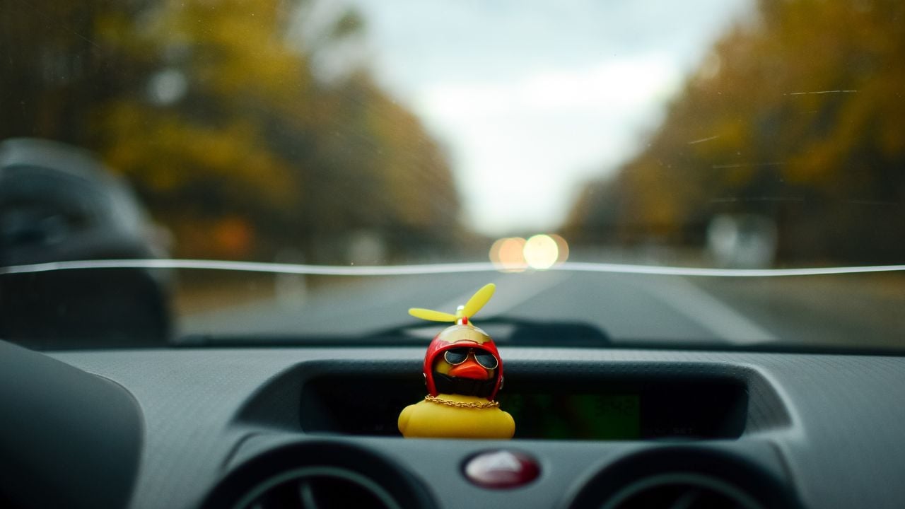 photo of the road from the interior of the car with bokeh,lights and a rubber duck.Travel by car.View from the car.Track.Car windshield.Beautiful landscape.Yellow duck.Dashboard. Auto driving.motion.