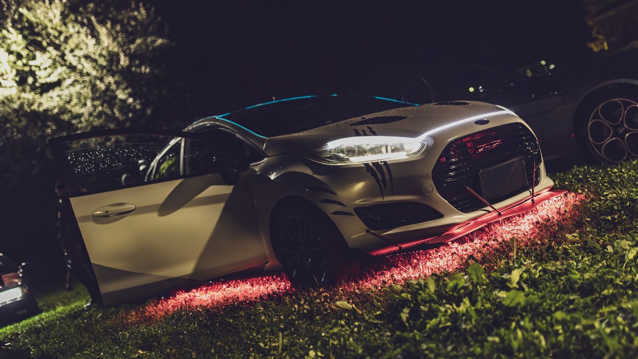 A silver ford fiesta parked on grass at night showing red underglow lights