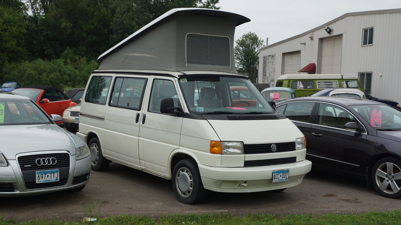 A Volkswagen Eurovan in white with the roof tent raised, front 3/4 view
