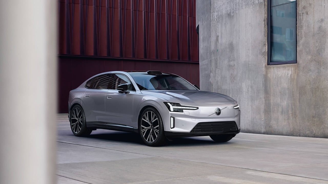 The Volvo ES90 next to some modern architecture, silver exterior, front 3/4 view