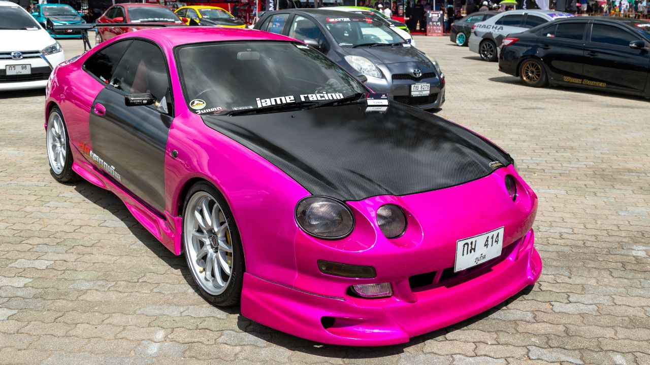 A modified pink Toyota Celica with carbon fiber parts.