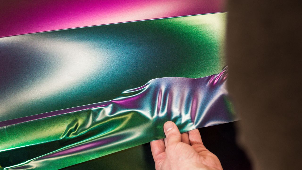 A specialist in wrapping a car with chameleon-colored vinyl film in the process of work. Car wrapping specialists cover the car with vinyl sheet or film