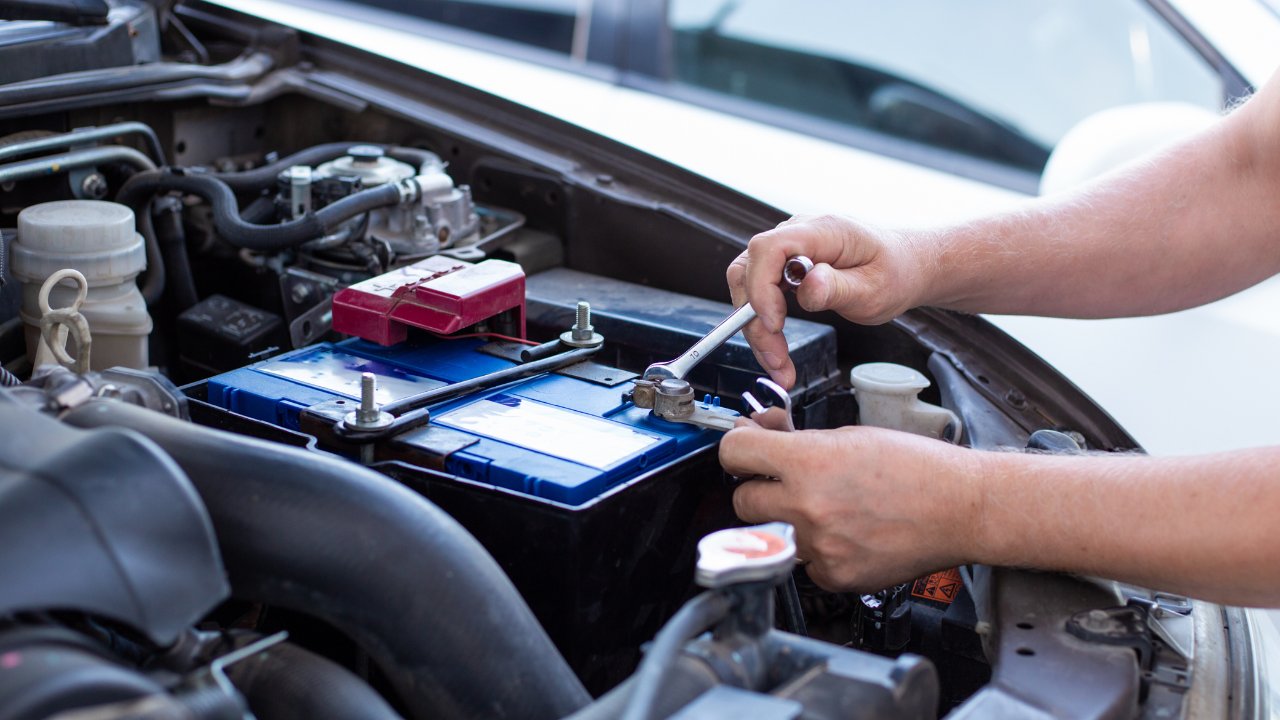 a man tightens with a wrench bolts for fastening a new battery, installing spare parts for a car