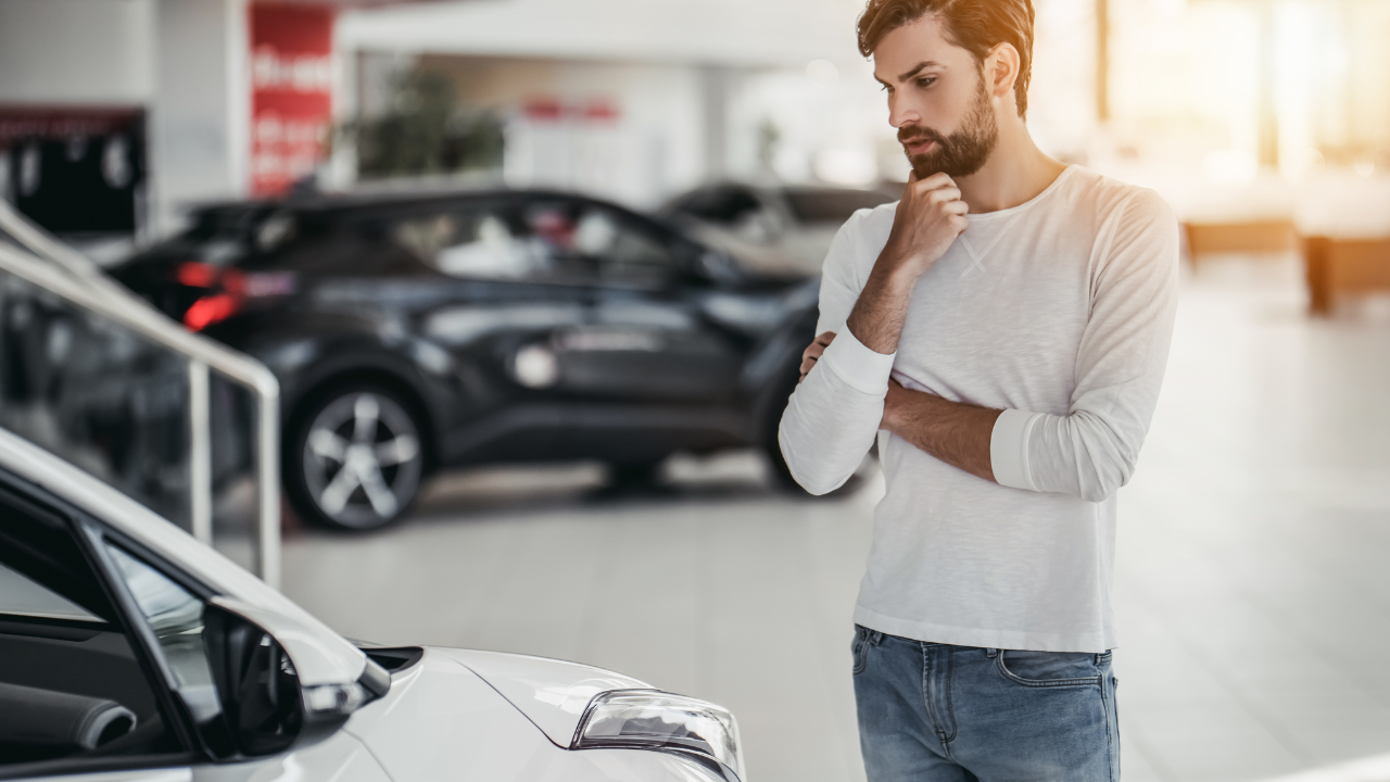 Young man is choosing a new vehicle in car dealership.