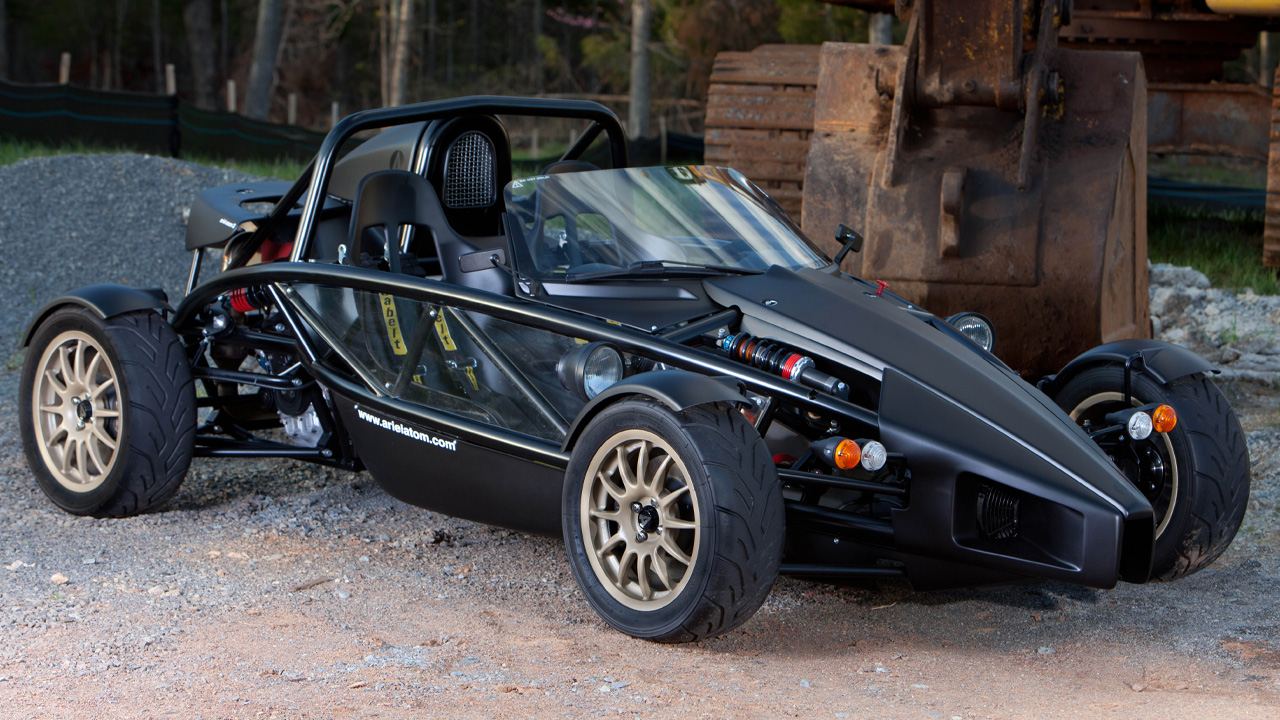 A black Ariel Atom with gold wheels, front 3/4 view