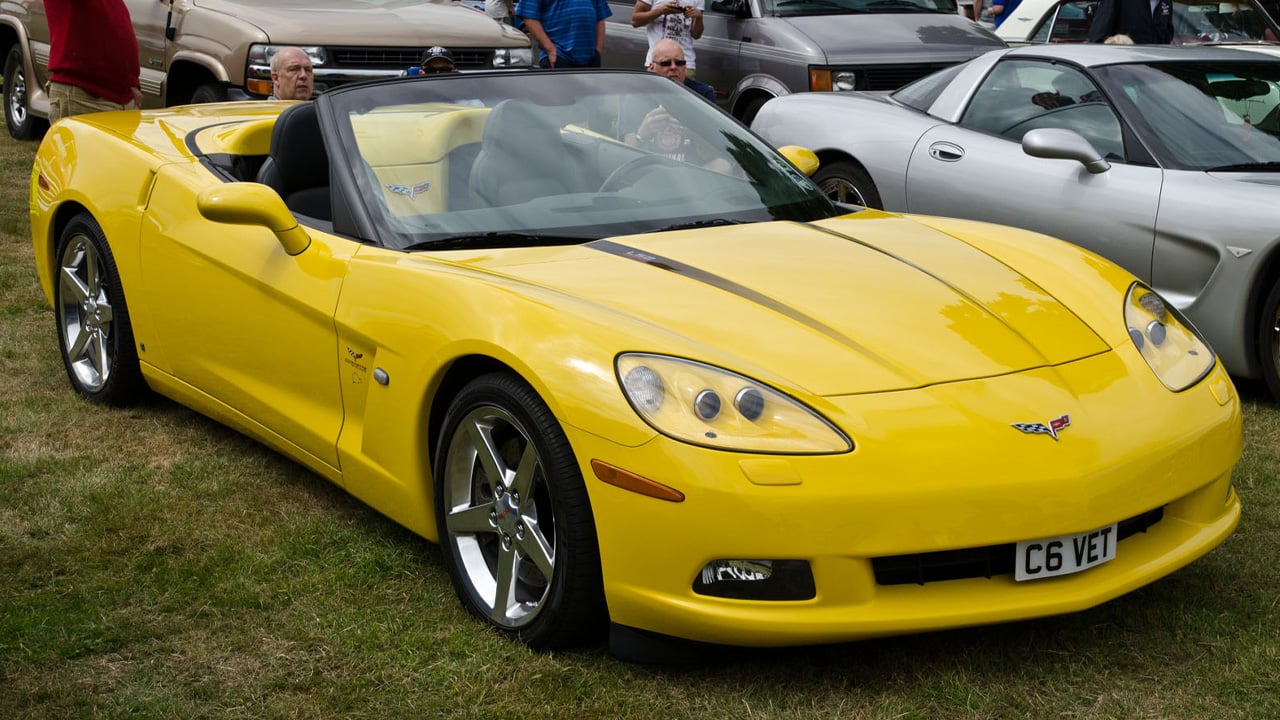 A yellow Chevrolet Corvette C6 Convertible at an open air car show, front 3/4 view