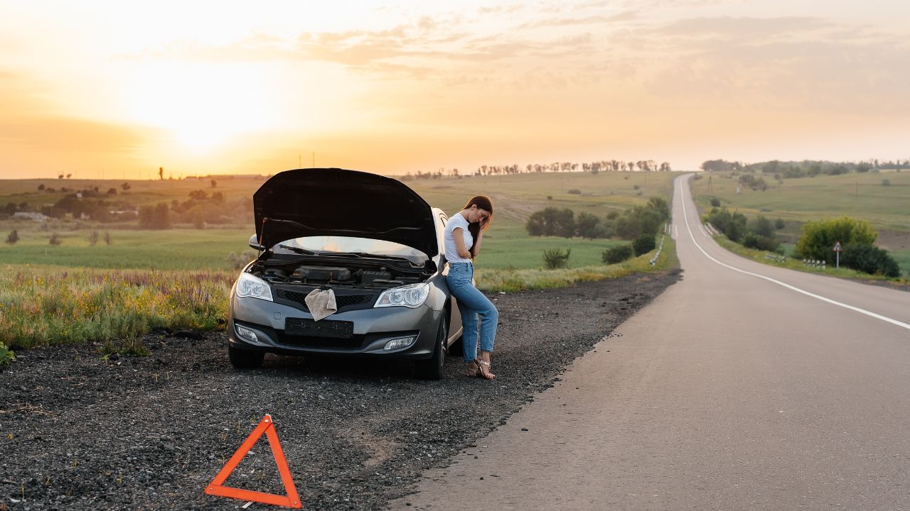 Woman next to broken down car on the highway in the dusk.