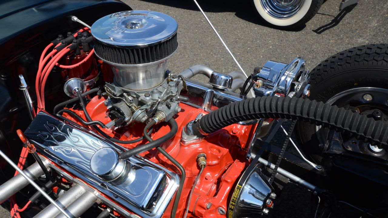 A customized, carbureted V8 hot rod engine with a red engine block and chrome valve covers.