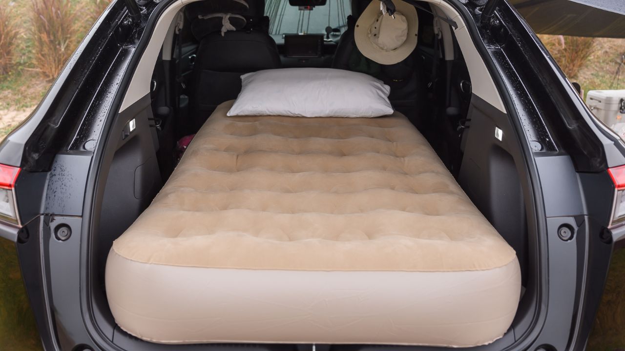 Camping in the car while on vacation with an inflatable mattress in the back, sleeping gear packed in the back door, and sleeping in her car while on vacation