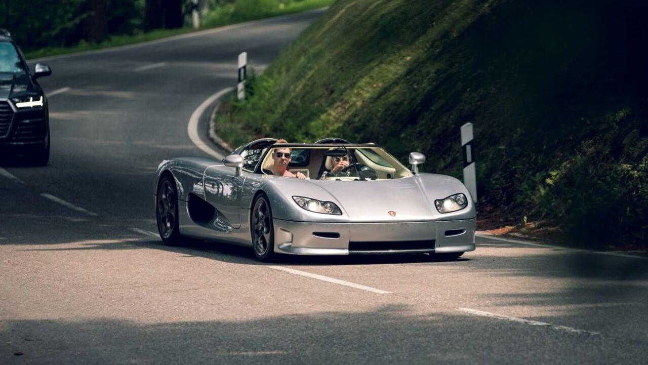 Silver Koenigsegg CC8S Driving Down The Road With Two Passangers Front 3/4 View