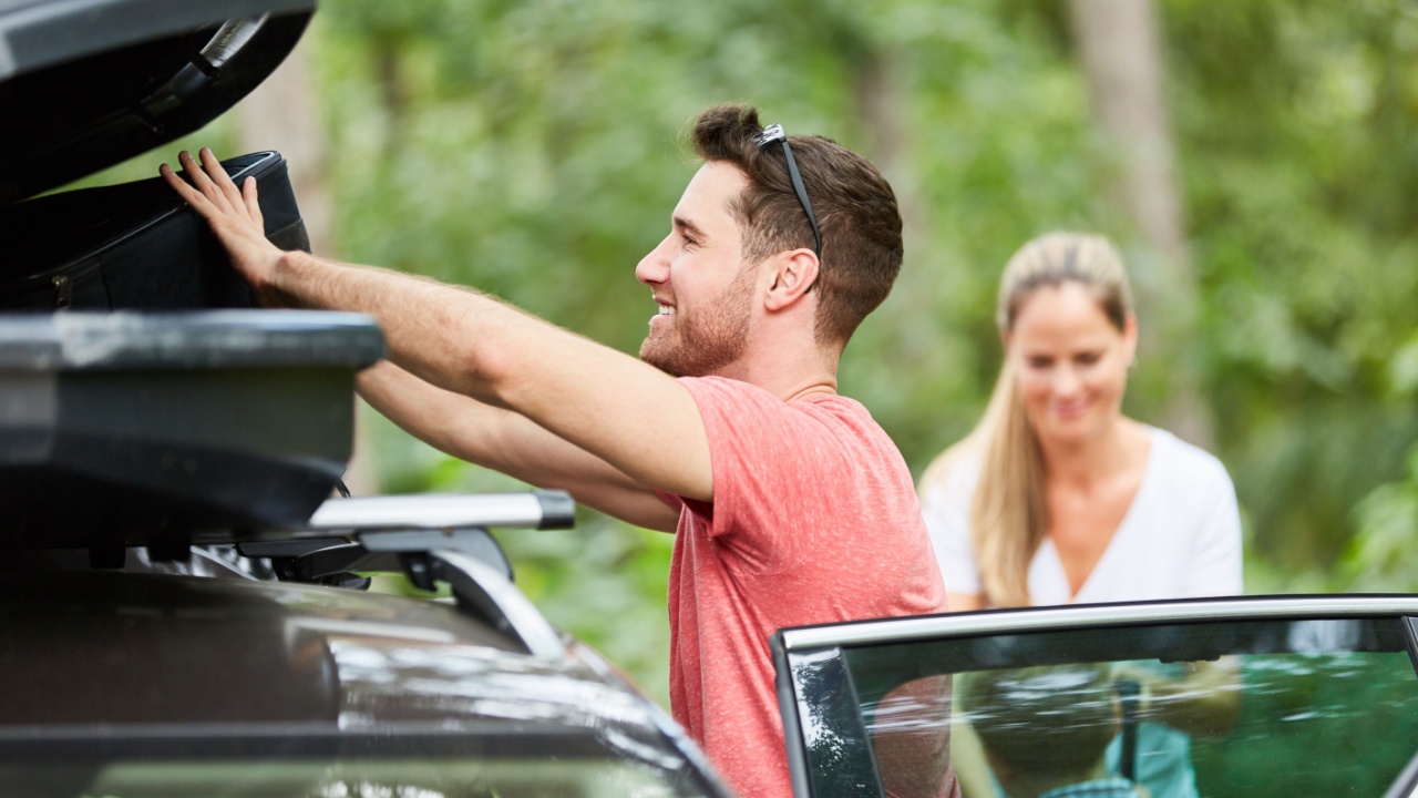 A man stows luggage in the roof box in the car before traveling on vacation