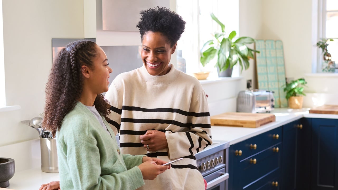 Mother and daughter talking in kitchen phone, celebrating excited